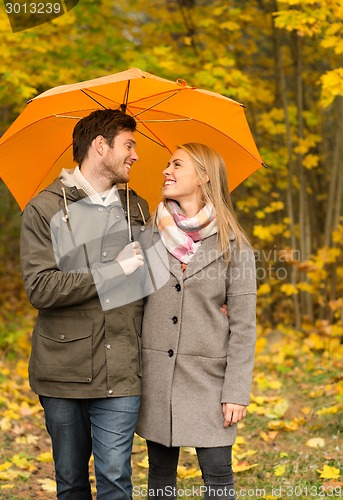 Image of smiling couple with umbrella in autumn park