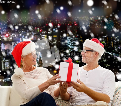 Image of happy senior couple in santa hats with gift box