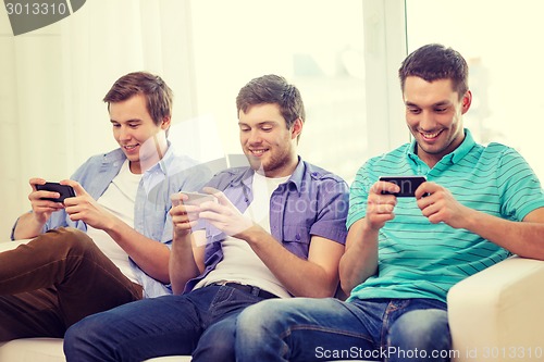 Image of smiling friends with smartphones at home