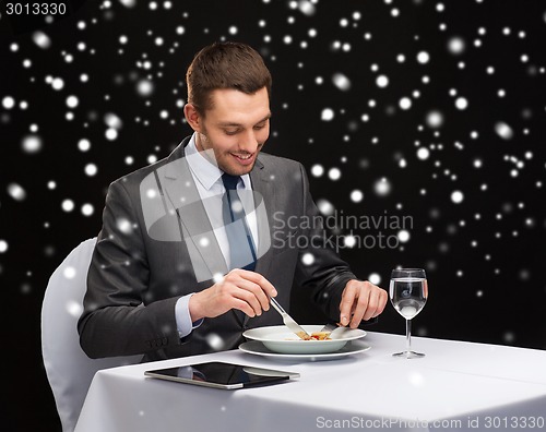 Image of smiling man with tablet pc eating main course