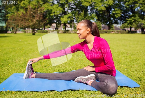 Image of smiling woman stretching leg on mat outdoors