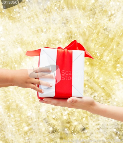 Image of close up of child and mother hands with gift box