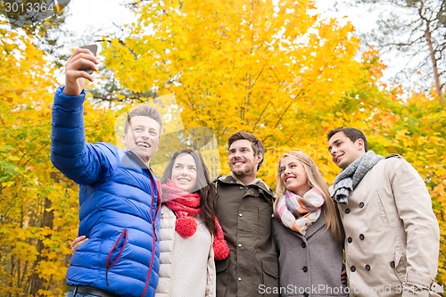 Image of smiling friends with smartphone in city park