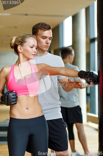 Image of smiling woman with personal trainer boxing in gym