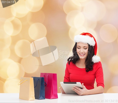 Image of smiling woman in santa hat with bags and tablet pc