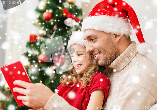 Image of smiling father and girl in santa hats reading book