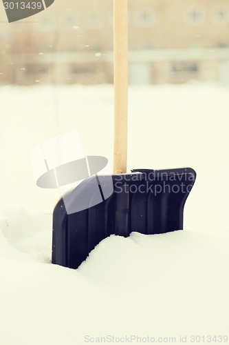 Image of black snowshowel with wooden handle in snow pile