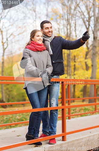 Image of smiling couple hugging on bridge in autumn park