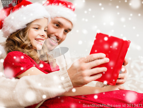 Image of smiling father and girl in santa hats reading book