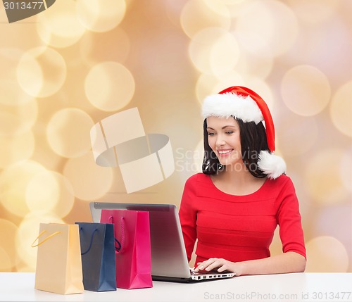 Image of smiling woman in santa hat with bags and laptop