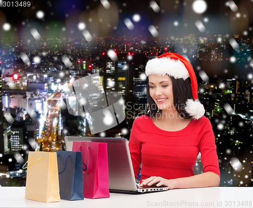Image of smiling woman in santa hat with bags and laptop