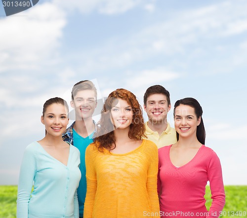 Image of group of smiling teenagers over blue sky and grass