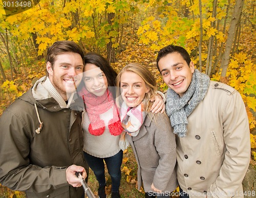 Image of smiling friends taking selfie in autumn park