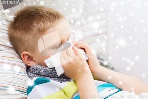 Image of ill boy blowing nose with tissue at home