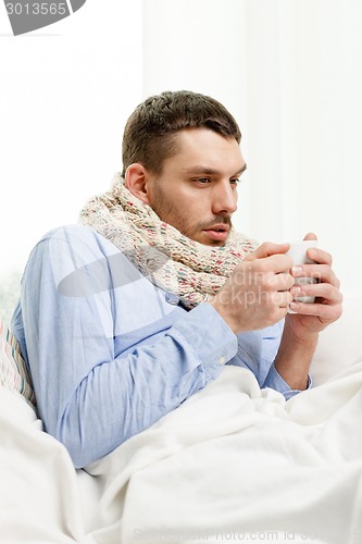 Image of man in scarf holding cup with hot drink at home