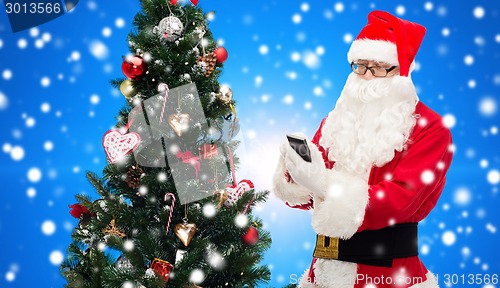 Image of santa claus with smartphone and christmas tree