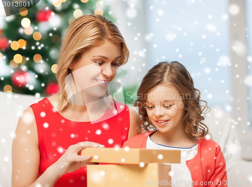 Image of smiling mother and daughter with gift box at home