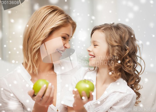 Image of happy mother and daughter holding green apples