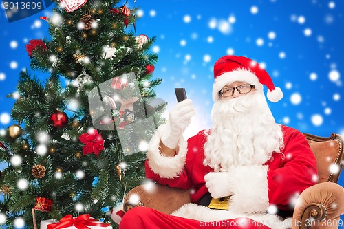 Image of santa claus with smartphone and christmas tree