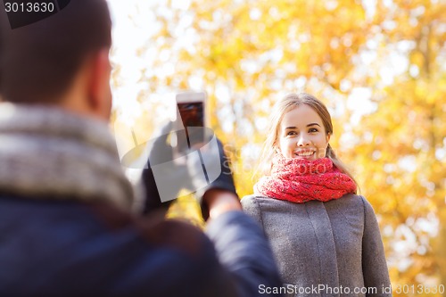 Image of smiling couple with smartphone in autumn park