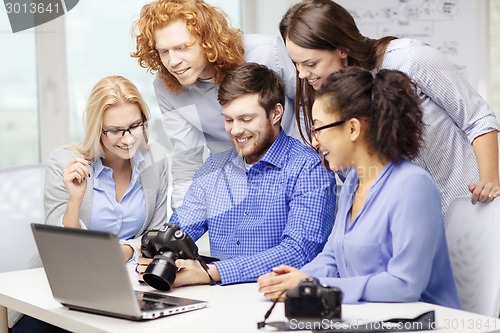 Image of smiling team with laptop and photocamera in office