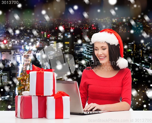 Image of smiling woman in santa hat with gifts and laptop