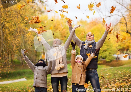 Image of happy family playing with autumn leaves in park