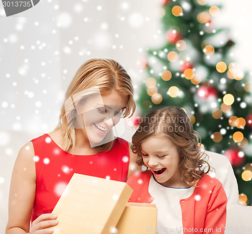 Image of smiling mother and daughter with gift box at home