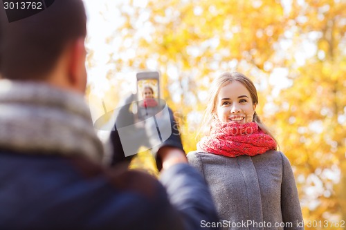 Image of smiling couple with smartphone in autumn park
