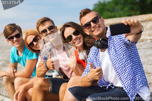 Image of group of smiling friends with smartphone outdoors