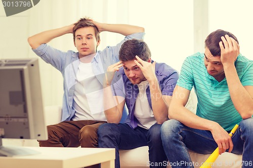 Image of sad male friends with vuvuzela watching sports