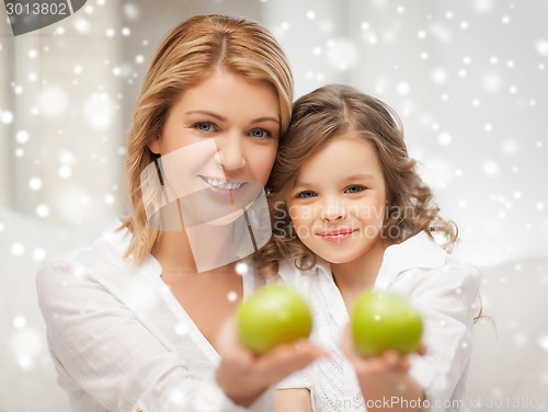 Image of happy mother and daughter holding green apples