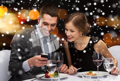 Image of smiling couple with smartphone at restaurant