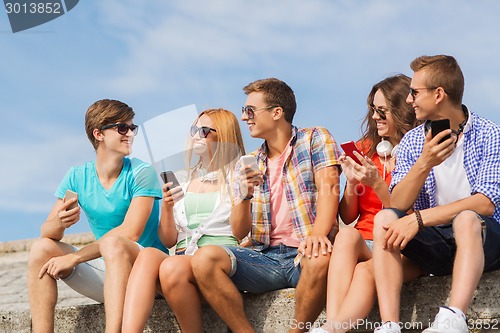 Image of group of smiling friends with smartphones outdoors