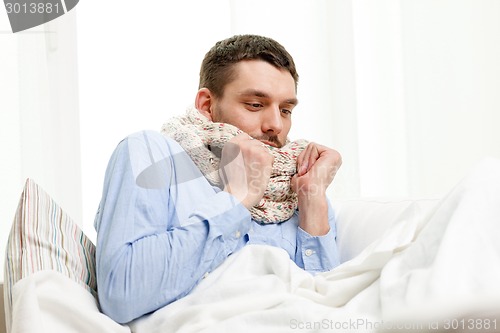 Image of ill man wearing scarf lying in bed at home