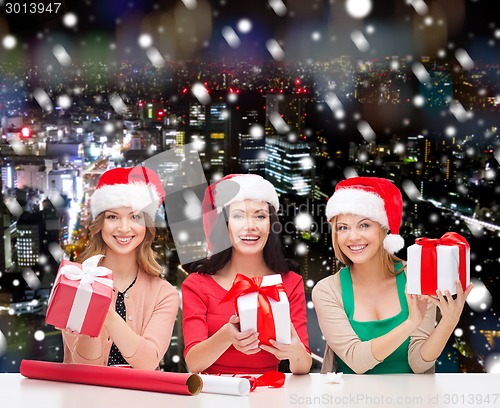 Image of smiling women in santa helper hats packing gifts