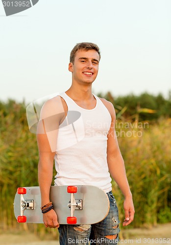 Image of smiling teenage boy with skateboard outdoors