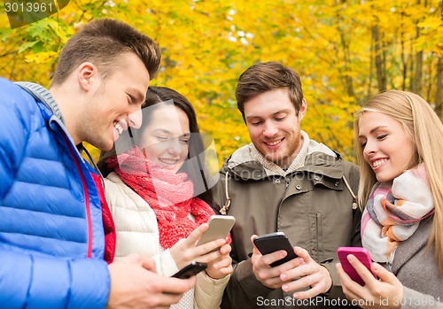 Image of smiling friends with smartphones in city park