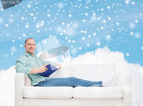 Image of smiling man with book lying on sofa