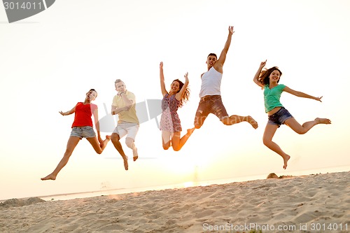Image of smiling friends dancing and jumping on beach