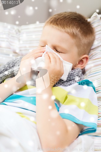 Image of ill boy blowing nose with tissue at home