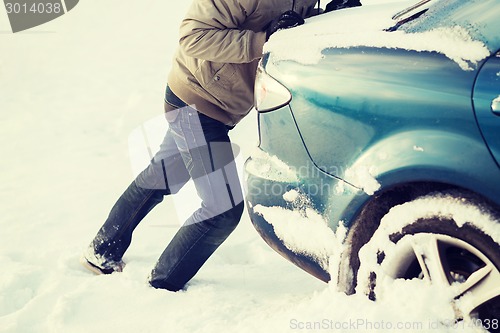 Image of closeup of man pushing car stuck in snow