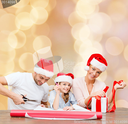 Image of happy family in santa helper hats packing gift