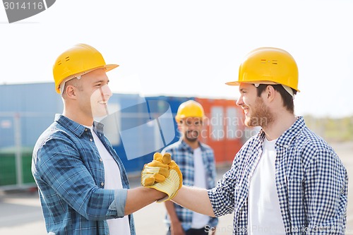 Image of group of smiling builders in hardhats outdoors