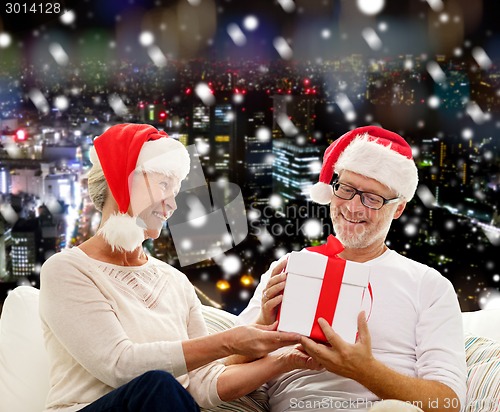 Image of happy senior couple in santa hats with gift box