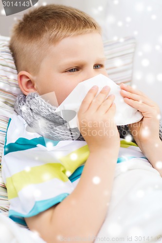 Image of ill boy blowing nose with tissue at home