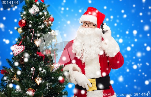 Image of santa claus with smartphone and christmas tree