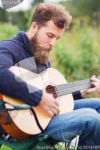 Image of man with beard playing guitar in camping