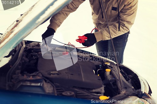 Image of closeup of man under bonnet with starter cables
