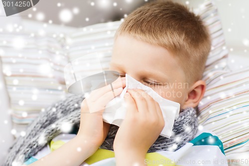 Image of ill boy blowing nose with tissue at home